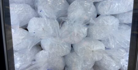 Large bags of ice stacked on top of each other inside a big cooler. Each bag is tied off neatly.