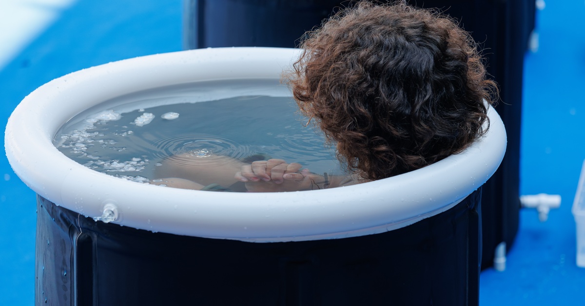 Someone sitting in an ice bath with their head turned away. They are covered in ice water from the neck down.