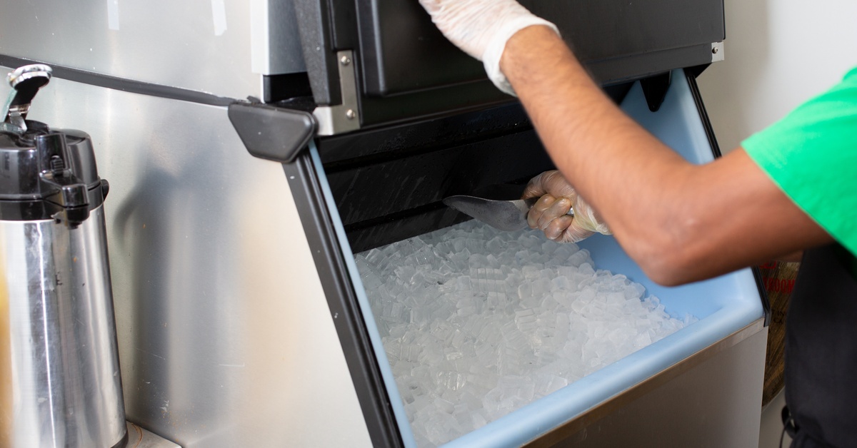 Someone wearing a latex glove holds open the door to an in-house ice machine. They scoop ice out from the middle.