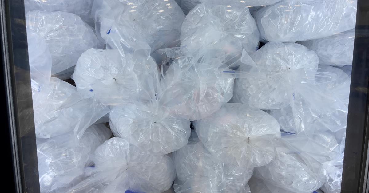 Several stacks of clear plastic bags filled with pieces of ice behind a glass door in a store freezer.