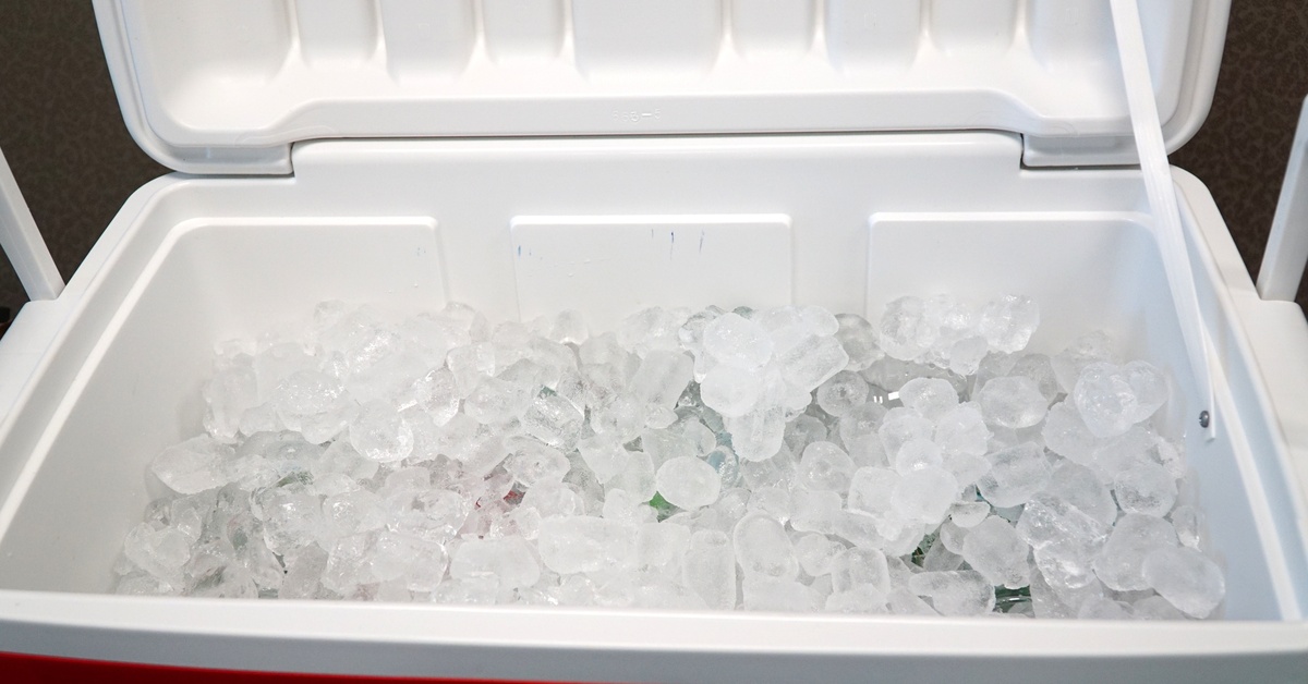 A close-up of a large red and white cooler with the lid open. Clear, clean ice rests in piles inside the cooler.