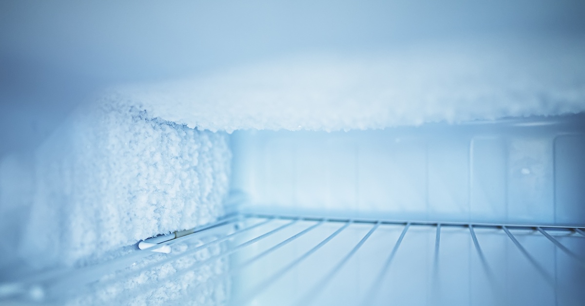 The inside of a small freezer. Ice crystals cover the walls and top of the freezer with a wire rack in the middle.