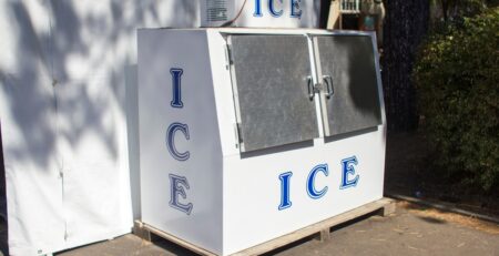 An ice freezer outside, sitting on a wooden pallet. The side, front, and top of the freezer say "ICE."