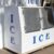 An ice freezer outside, sitting on a wooden pallet. The side, front, and top of the freezer say "ICE."