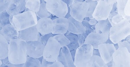A close-up pile of translucent ice cubes, frosty and slightly rounded, with a hole in the middle.