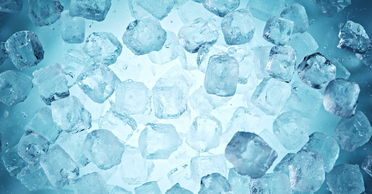 An overhead view of scattered clear ice cubes floating in blue water, with a bright center glow and tiny bubbles.
