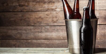 A few bottles inside a metal bucket with one resting in front of it. Condensation is on the bottles and bucket.