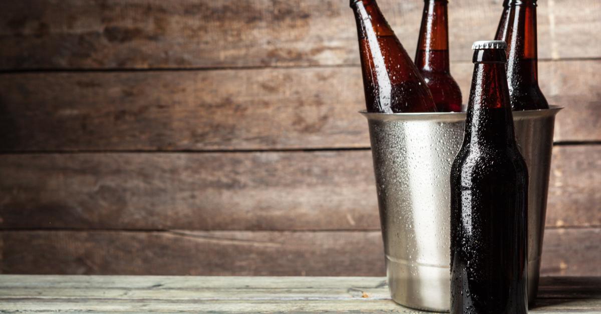 A few bottles inside a metal bucket with one resting in front of it. Condensation is on the bottles and bucket.