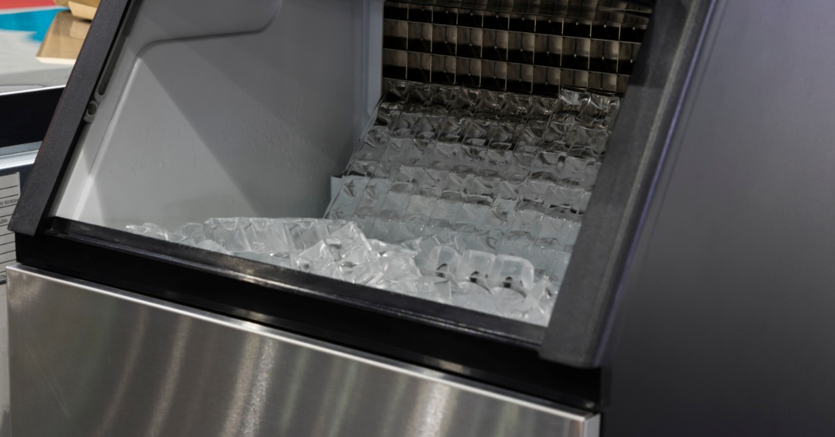An ice machine with the door open and a low supply of ice. A fresh batch of ice is coming out of the machine.