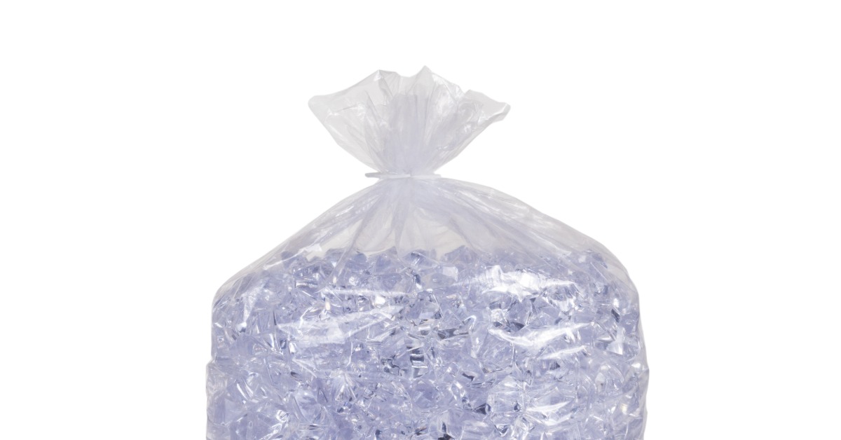 A full bag of fresh ice that is tied off at the top with a plastic tie. The bag rests against a white background.