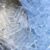 A close-up of a metal scoop immersed in a pile of ice cubes. The ice cubes are cylindrical with a hole in the middle.