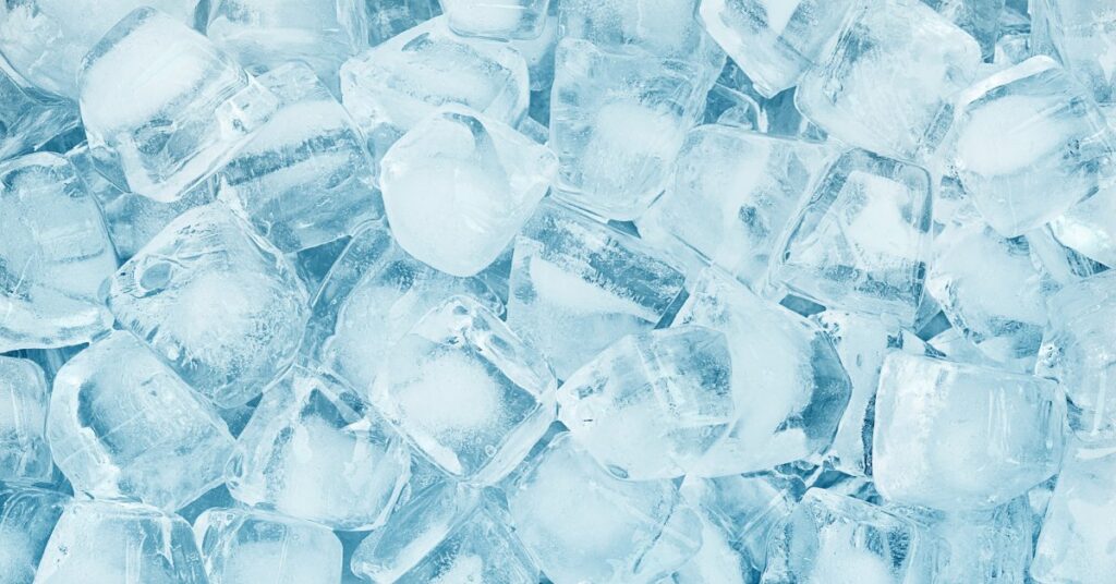 A close-up of a pile of ice cubes. The ice cubes have a blue tint and random cracks and air pockets.