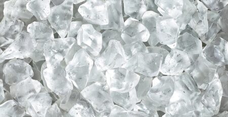 A close-up of a large pile of fresh, clean ice cubes. Tiny water droplets are on the melting cubes.