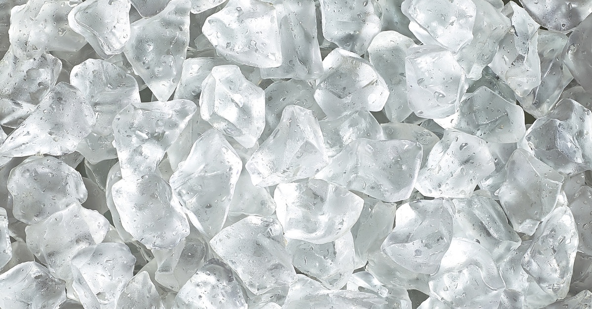A close-up of a large pile of fresh, clean ice cubes. Tiny water droplets are on the melting cubes.