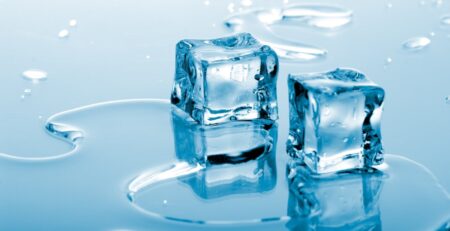 Two melting ice cubes sit in a shallow pool of water as smaller ice pieces blur across the cool blue background.