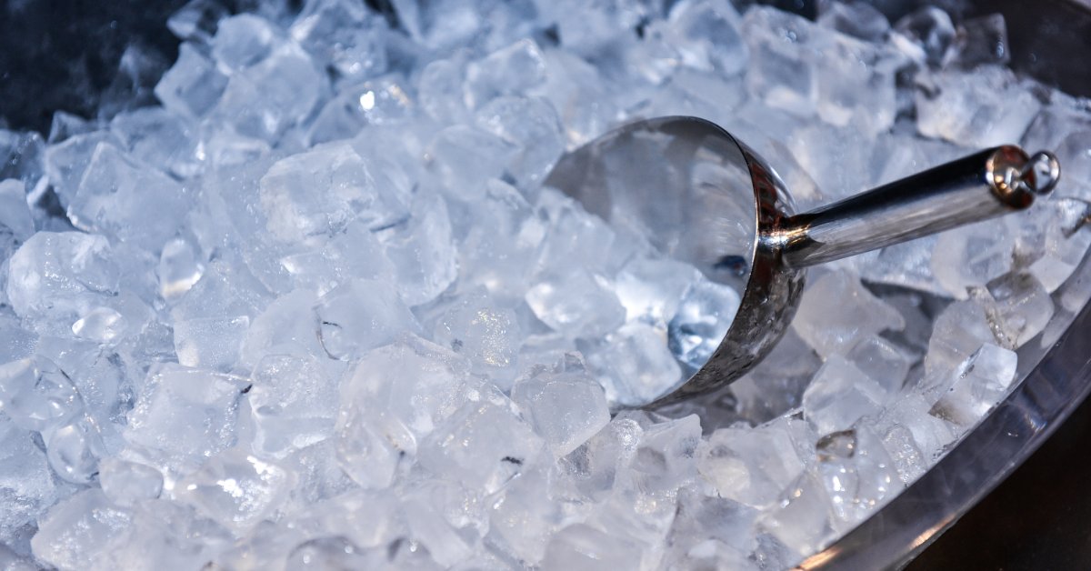 A polished metal scoop rests in a large container filled with clear ice cubes prepared for beverage service.